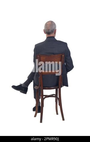 back view of a man sitting  on chair with suit and tie and cross legged  on white background Stock Photo