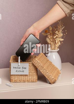 Woman putting phone into box with different gadgets at home Stock Photo