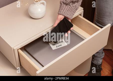 Woman putting her phone in drawer with different gadgets at home Stock Photo