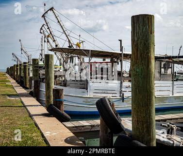 ROCKPORT, TX - 14 FEB 2023: A row of wooden pilings at the marina with moored fishing boats on a partly sunny day in Texas. Stock Photo