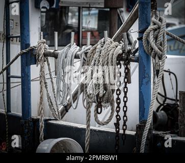Several used ropes and a chain hanging on the deck of a commercial fishing boat. Stock Photo
