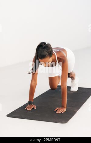 Young slim woman in white sportswear doing core exercises. Female doing cardio exercises on mat outdoors. Stock Photo