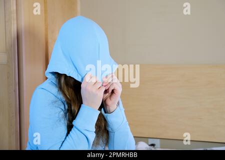 protest teenager girl teenager put a hood on her face pull a hood over her eyes in room in the bedroom sitting alone sad crying suffering psychological problems of a child in adolescence Stock Photo