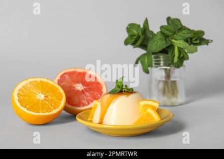 Plate with delicious pudding, mint and orange pieces covered by caramel syrup on grey background Stock Photo
