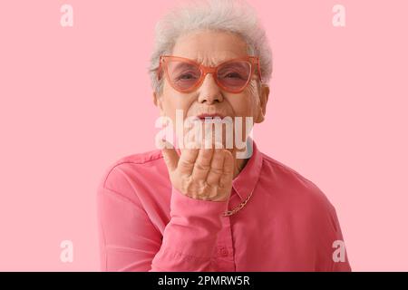 Senior woman blowing kiss on pink background, closeup Stock Photo