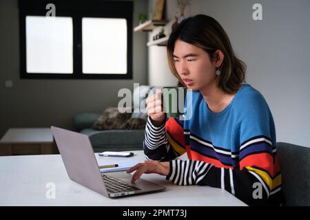 Taiwanese man drinking coffee while working at home with a laptop. Stock Photo