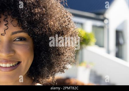 Half face portrait of happy biracial woman smiling and looking to camera in sunny garden, copy space Stock Photo