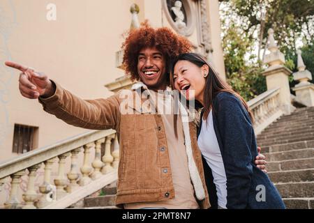 Young multiracial couple walking and having fun on a romantic trip pointing monument. African american boyfriend and chinese girlfriend smiling bonding together sightseeing with affectionate attitude. High quality photo Stock Photo