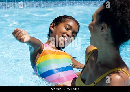 Happy biracial mother and daughter playing in sunny outdoor swimming pool Stock Photo