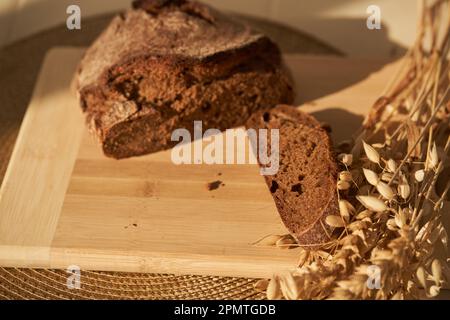 Fresh, brown, freshly baked, multi-grain and yeast-free bread on a cutting board and cereals, cut off a piece of the bread separately and copy space. Sun lights and shadows. High quality photo Stock Photo