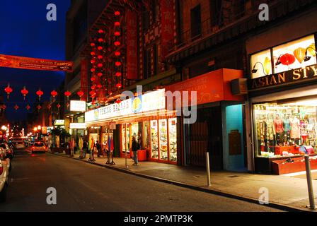Chinese lanterns are strung across a street and illuminated at night in front of the stores in the Chinatown district in San Francisco Stock Photo