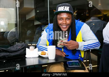 A young man in a bright blue and yellow jacket is seated at a table with a tablet Stock Photo