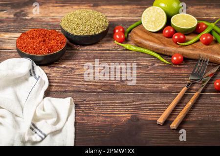 Empty wooden cutting board with copy space surrounded by peppers, herbs, tomatoes, lemon and other delicious flavored vegetables on table Stock Photo