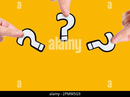 Close-up view of three white and black plastic question marks in hands isolated on plain yellow background with copy space. The concept of curiosity, Stock Photo