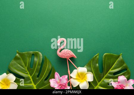 Exotic jungle summer frame. Summer beach party concept. Pink flamingo, tropical leaf monstera and orchid flowers on green background. Flat lay, copy s Stock Photo