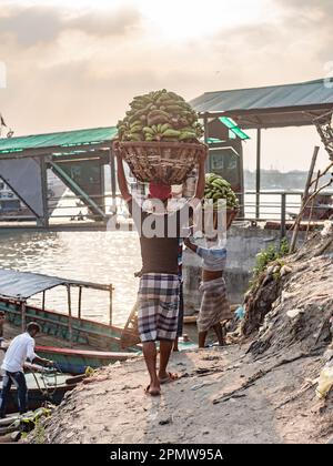 Men carrying bunches of green bananas to local ferries at Wise Ghat Boat Station on Buriganga River in Dhaka, the capital of Bangladesh. Stock Photo