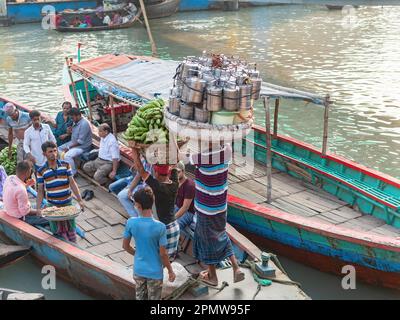 Men carrying bunches of green bananas and other products to local ferries at Wise Ghat Boat Station on Buriganga River in Dhaka, the capital of Bangla Stock Photo