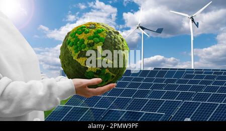 Woman holding a green planet Earth on a background of wind turbines and solar panels. Stock Photo