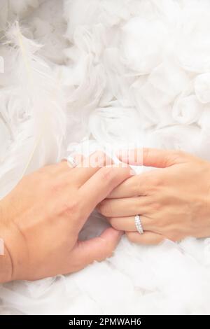 Man and woman newlyweds couple with wedding ring on left ring finger and angel white feather soft background Stock Photo