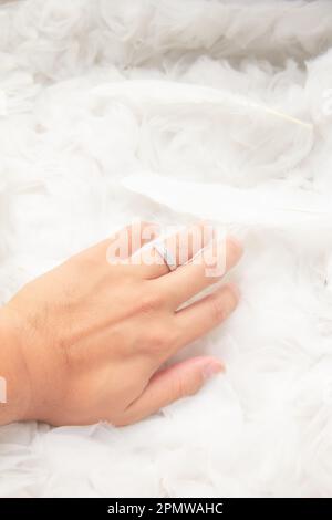 Man and woman newlyweds couple with wedding ring on left ring finger and angel white feather soft background Stock Photo