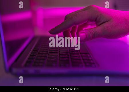 Person typing at laptop computer at night. Female uses keyboard, shakes buttons with fingers. Internet security, cyber attack. Trendy neon light. Crea Stock Photo