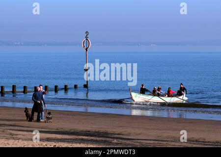 Edinburgh, Scotland, UK. 15th April 2023. Some early morning activity on Portobello beach with people enjoying the mild start to the day with blue sky and sunshine.  Wooden row boat about to land on the beach. Credit: Craig Brown/Alamy Live News Stock Photo