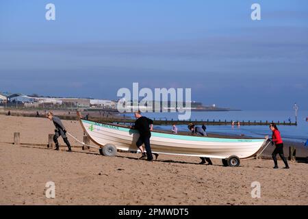 Edinburgh, Scotland, UK. 15th April 2023. Some early morning activity on Portobello beach with people enjoying the mild start to the day with blue sky and sunshine.  Transporting a wooden row boat up the beach. Credit: Craig Brown/Alamy Live News Stock Photo