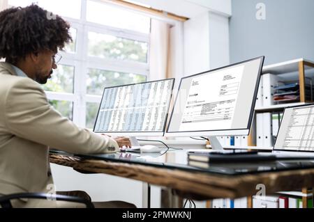 Looking At Invoice And Spreadsheet On Computer At Work Stock Photo