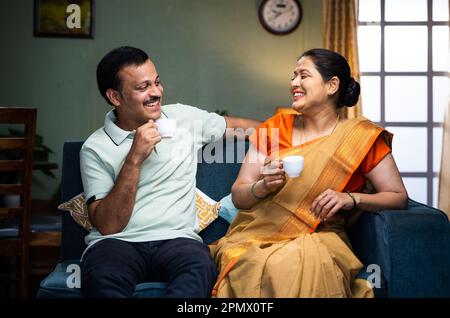 Happy smiling couple having tea or coffee while talking each other at home during morning - concept of family time, relaxation and refreshment Stock Photo