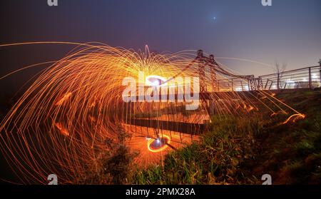 A striking photo of sparks from steel wool creating a dazzling effect on a metallic bridge at dusk Stock Photo