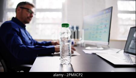Water Bottle On Desk And Man In Background Using Computer Stock Photo