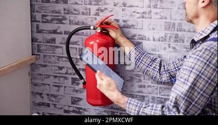 Worker Installing Fire Extinguisher. Inspection Service. Checking Security Label Stock Photo