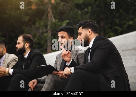 Business people outdoor meeting. Several men in suits sit on the steps of a street staircase during a work break. Successful promotion and recognition Stock Photo