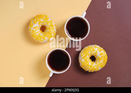 Directly above view of two cup of coffee and yellow donuts on two-tone background Stock Photo