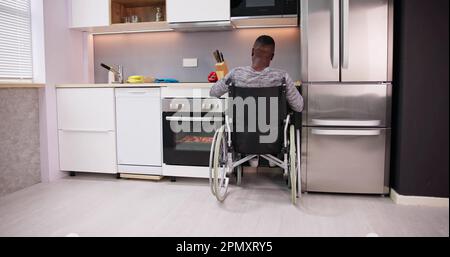 Young Disabled Man Sitting On Wheel Chair Preparing Food In Kitchen Stock Photo