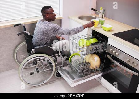 Young Man Sitting On Wheelchair Arranging Plates In Dishwasher Stock Photo
