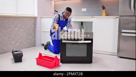 Young Male Repairman Repairing Oven In Kitchen Stock Photo