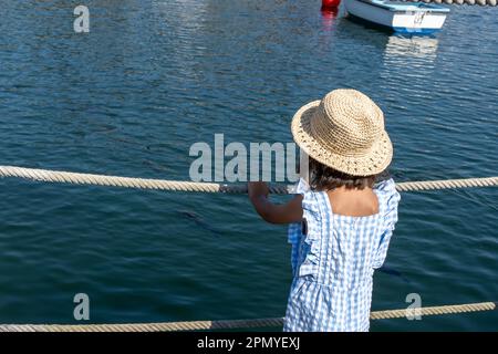 little girl in a straw hat in the harbour looking at the boats and