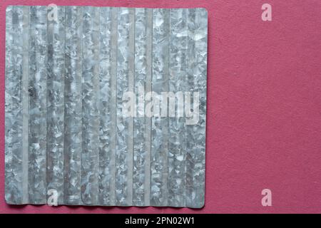 corrugated galvanized sheet metal shape (used for crafting) on rough pink red scrapbook paper Stock Photo
