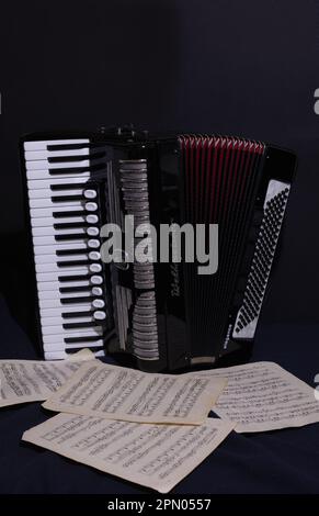 Weltmeister piano accordion with red bellows and a scatter of musical score in a dark setting Stock Photo