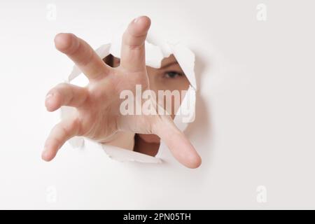 woman grabbing with hand through hole in paper wall Stock Photo