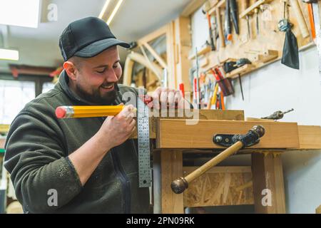 Happy male carpenter marking on wood with big pencil. Variety of tools used in carpentry - bracket and vise. High quality photo Stock Photo