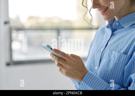 Smiling business woman using mobile phone standing in office, close up. Stock Photo