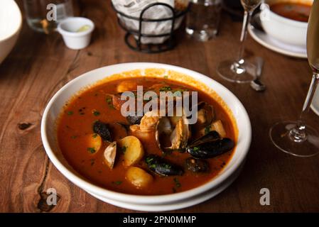 Steamed mussels in white plate with tomatoes, potatoes and bread, garnished with garlic in a restaurant setting Stock Photo