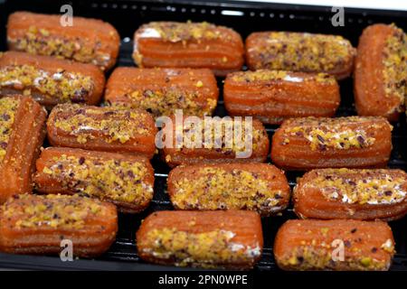 Tulumba, Bamiyeh or Balah El Sham stuffued with whipped cream and covered with pistachios and nuts, deep fried batter dessert soaked in syrup, similar Stock Photo