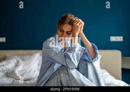 Young unhappy woman sitting on bed at home waking up depressed feeling sad and miserable Stock Photo