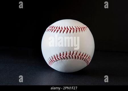 Close-up of a white baseball with red stitching on a black background Stock Photo
