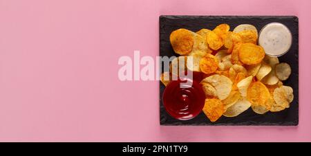 Perfectly salted and crispy potato chips with creamy white and savory red dip on pink background Stock Photo
