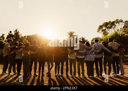 Back view of happy multigenerational people having fun in a public park during sunset time - Community and support concept Stock Photo