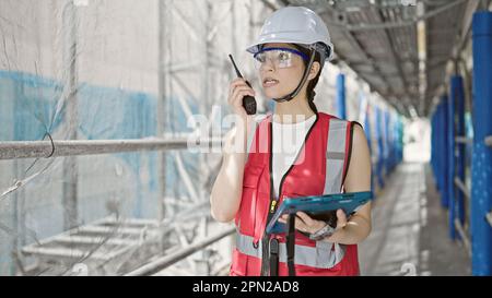 Young beautiful hispanic woman builder talking on walkie talkie using touchpad at street Stock Photo